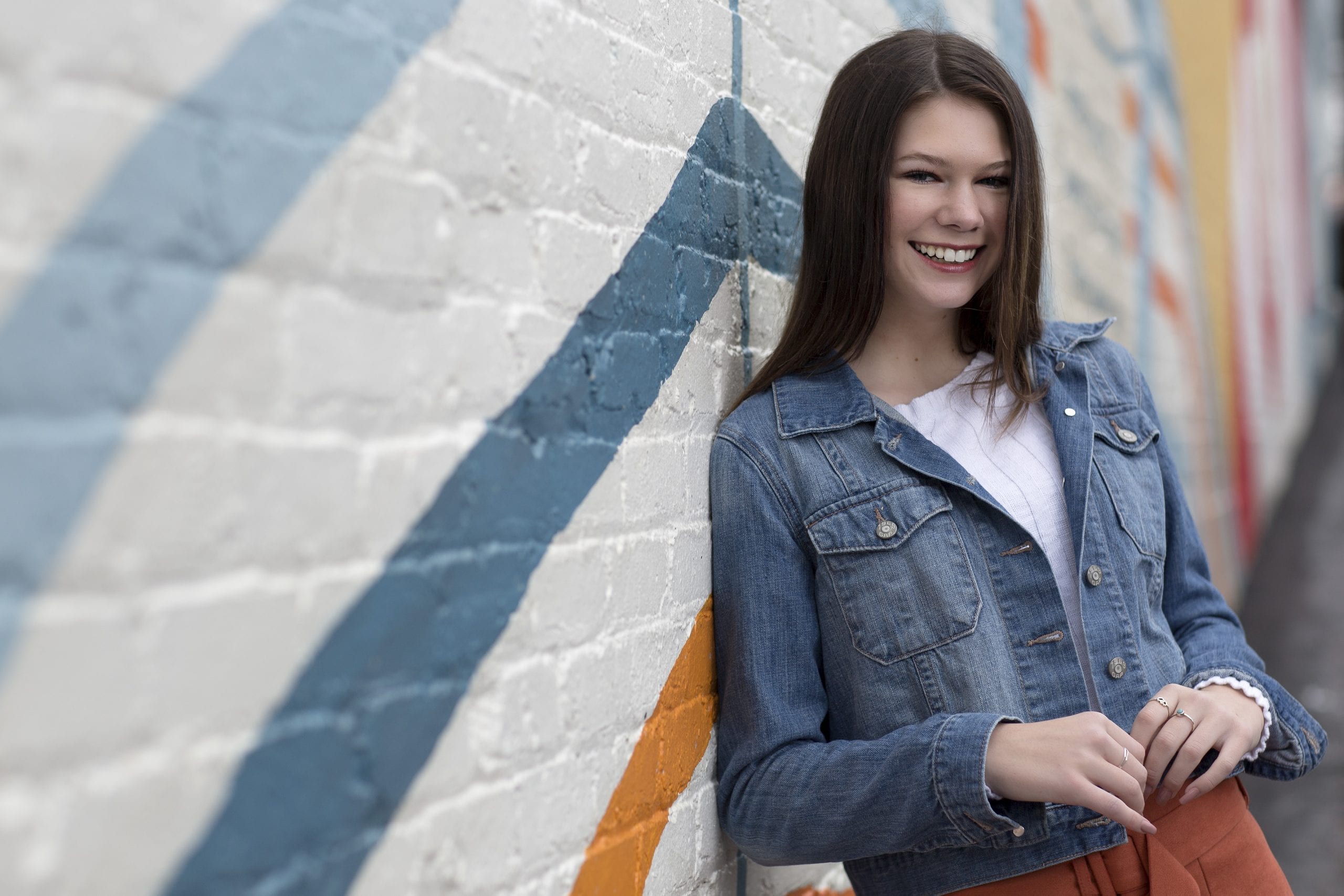 teen in jean jacket leaning against mural